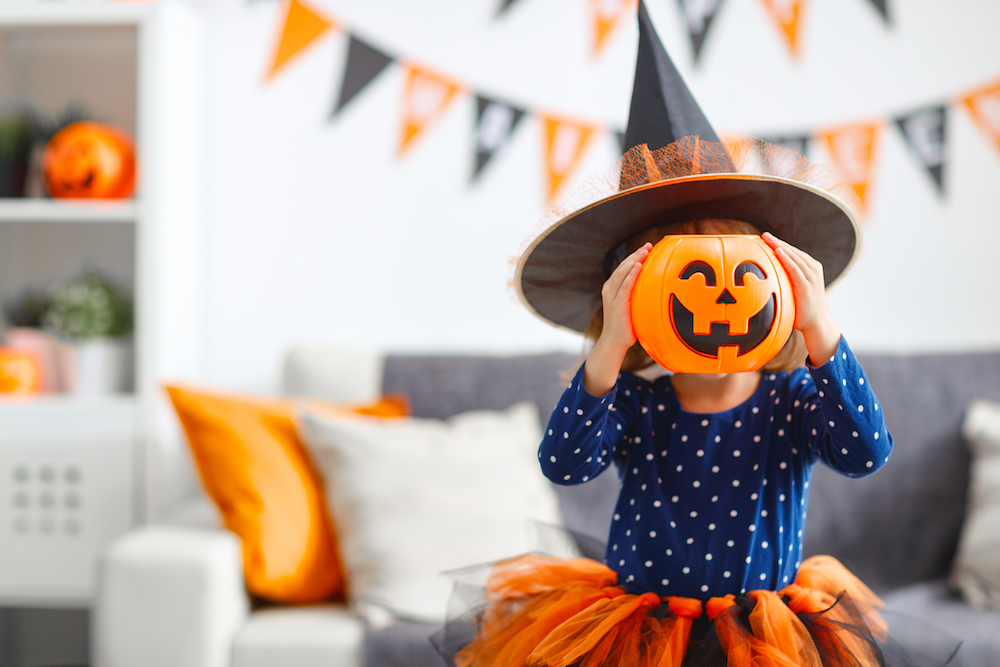 a young preschool aged girl holding a pumpkin mask above her head as she prepares her halloween costume