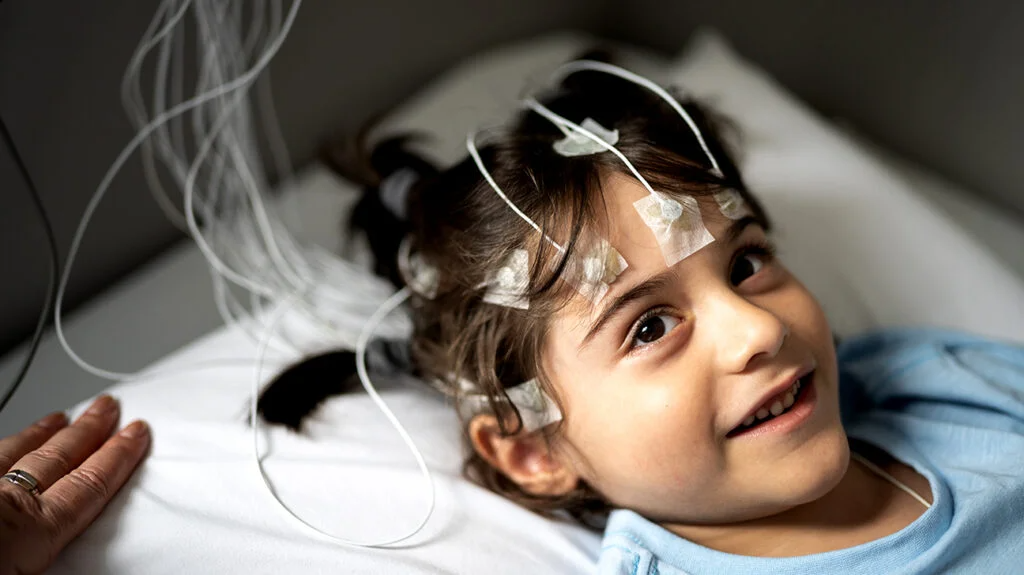 photograph that depicts a smiling child connected to an EEG machine
